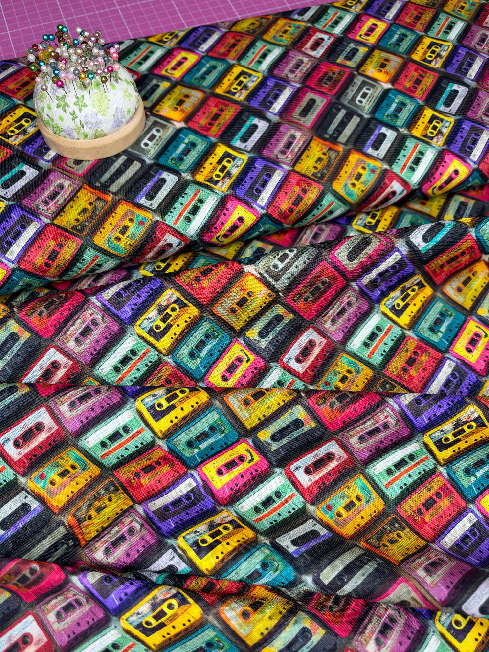 A close-up of multicolored fabric printed with a repeating pattern of vintage cassette tapes in many bright colors.