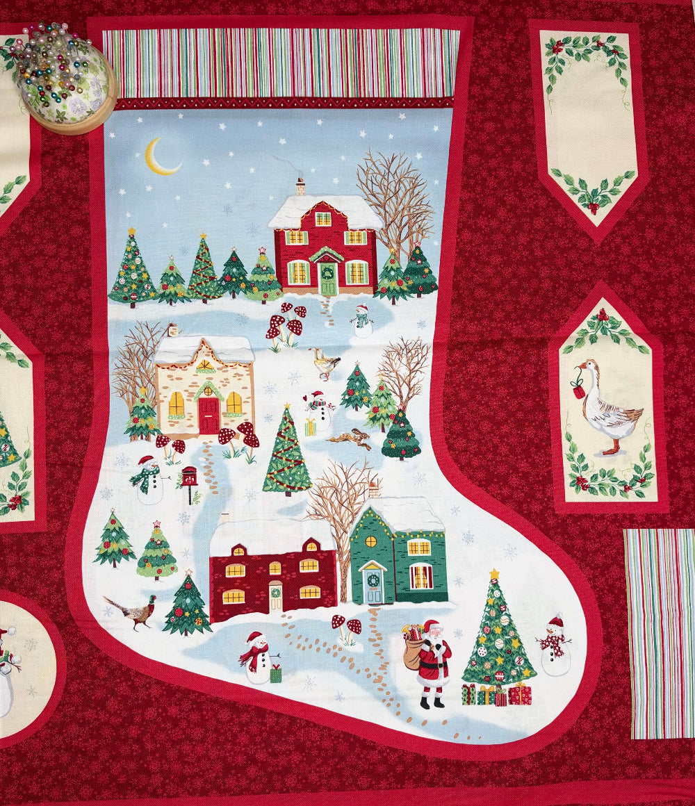 A Christmas-themed quilt pattern featuring a large stocking in the center with a winter village scene, surrounded by red patterned borders and additional decorative panels with holiday motifs.