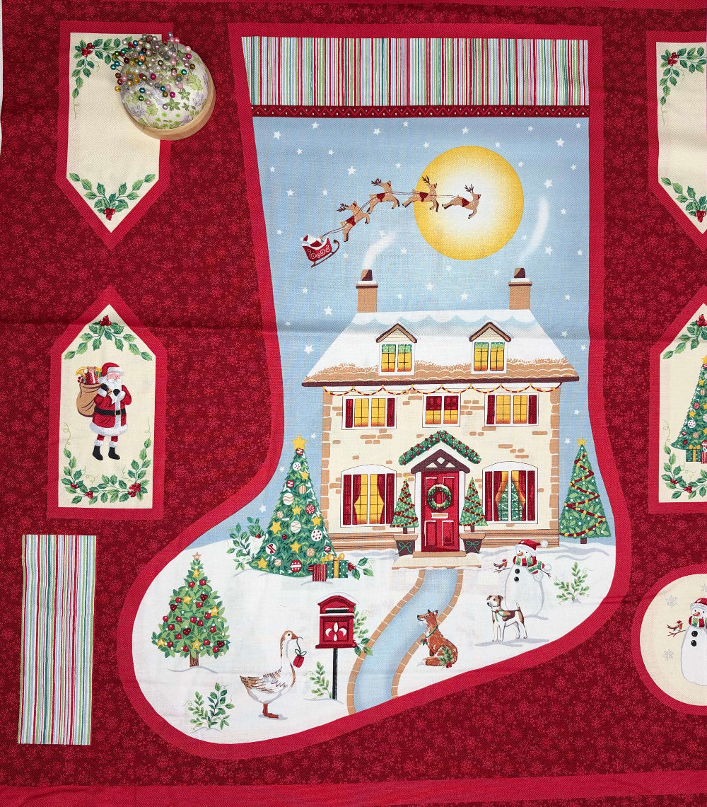 A Christmas-themed fabric design featuring a large red stocking outline with a winter village scene inside, including Santa, Rudolph the Red-Nosed Reindeer, a snowy house, Christmas trees, snowmen, and small animals. The design includes inset panels with holiday motifs on a red patterned background.