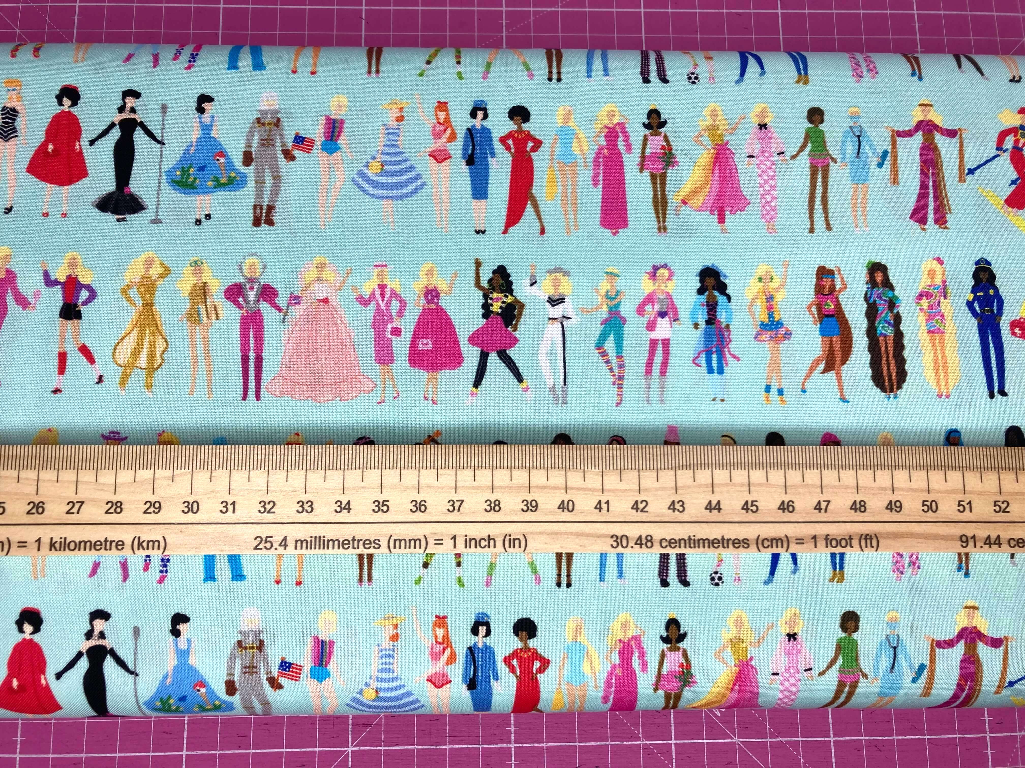 colourful barbie dolls on a powder blue cotton with a ruler