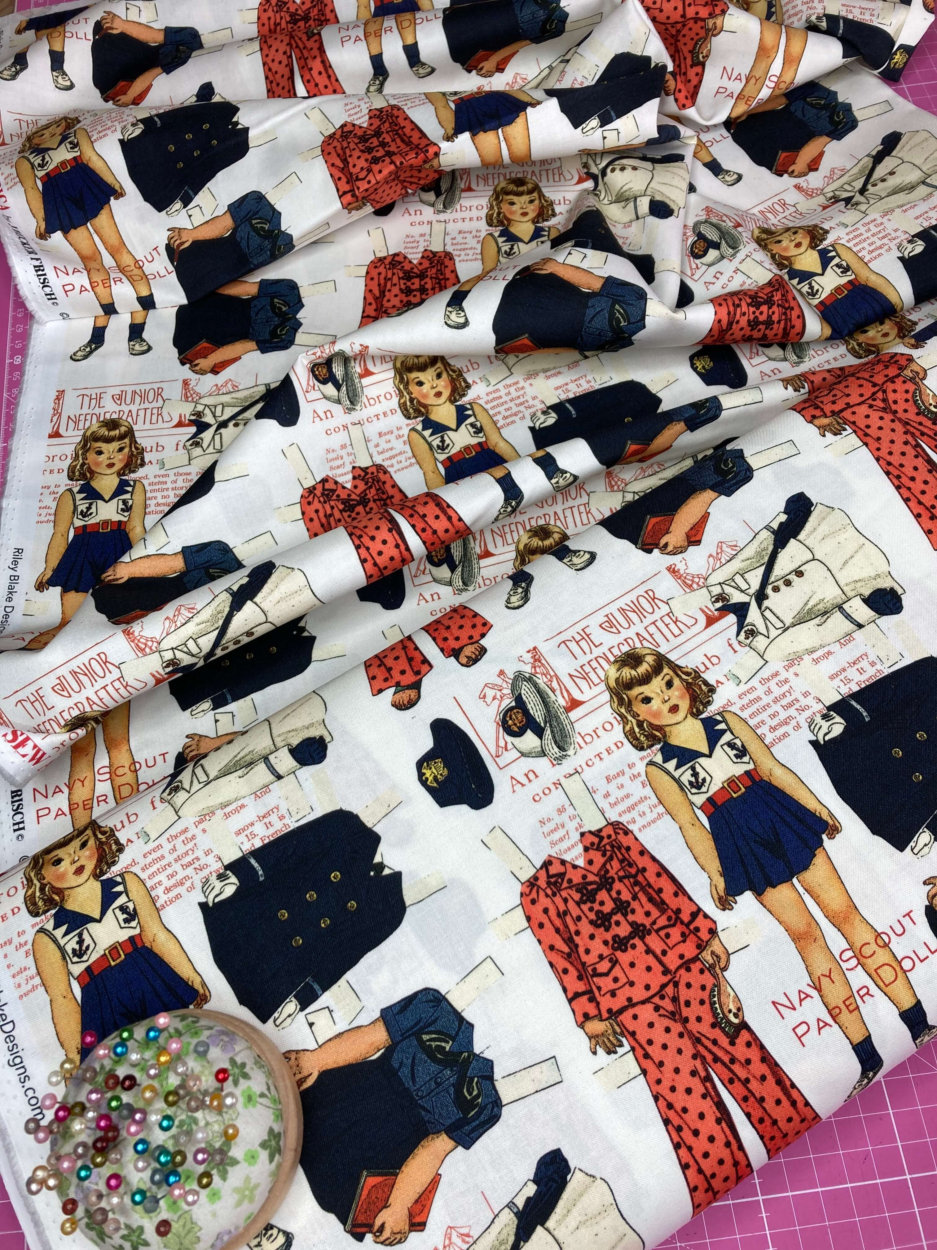 Fabric with vintage-style illustrations of dolls and clothing on a white background